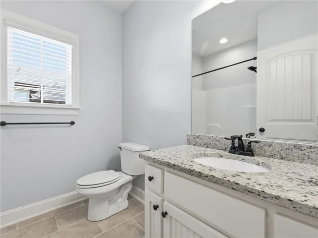 This bright bathroom features a spacious vanity with elegant granite countertops and a window for natural light.