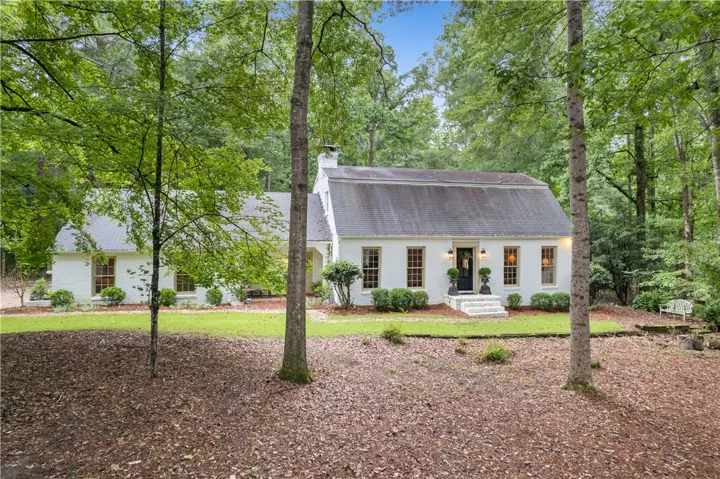 Nestled among trees, this inviting white brick residence features a welcoming front entry and lush landscaping.