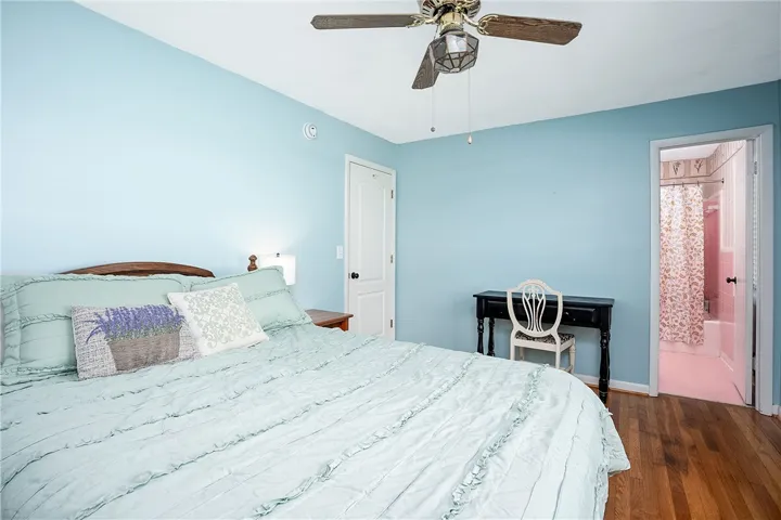 This cozy bedroom features hardwood floors and a bright, inviting atmosphere leading to an en-suite bathroom.