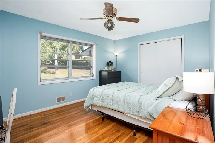 This cozy bedroom features polished hardwood floors and ample natural light from a large window.