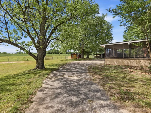 A gravel driveway leads to a serene property featuring a charming screened porch and mature trees.