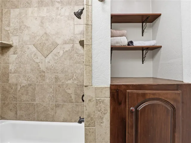 This bathroom features a shower with tiled walls and a built-in storage cabinet.