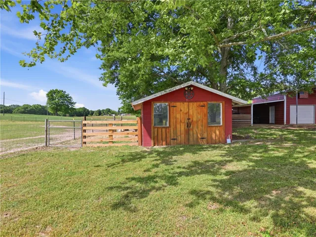 This vibrant red outbuilding with wooden doors offers versatile space amidst a lush, green landscape.