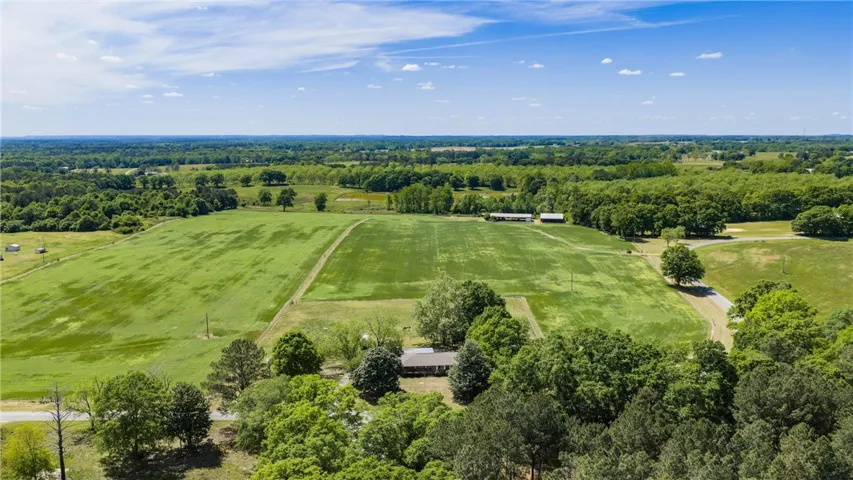 This expansive rural property offers sweeping green fields, mature trees, and outbuildings under bright skies.
