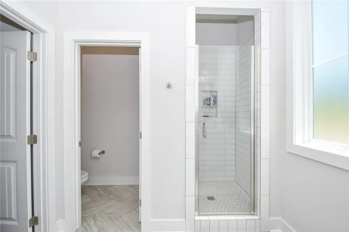 This bathroom features a contemporary shower with tile surround and a convenient water closet.