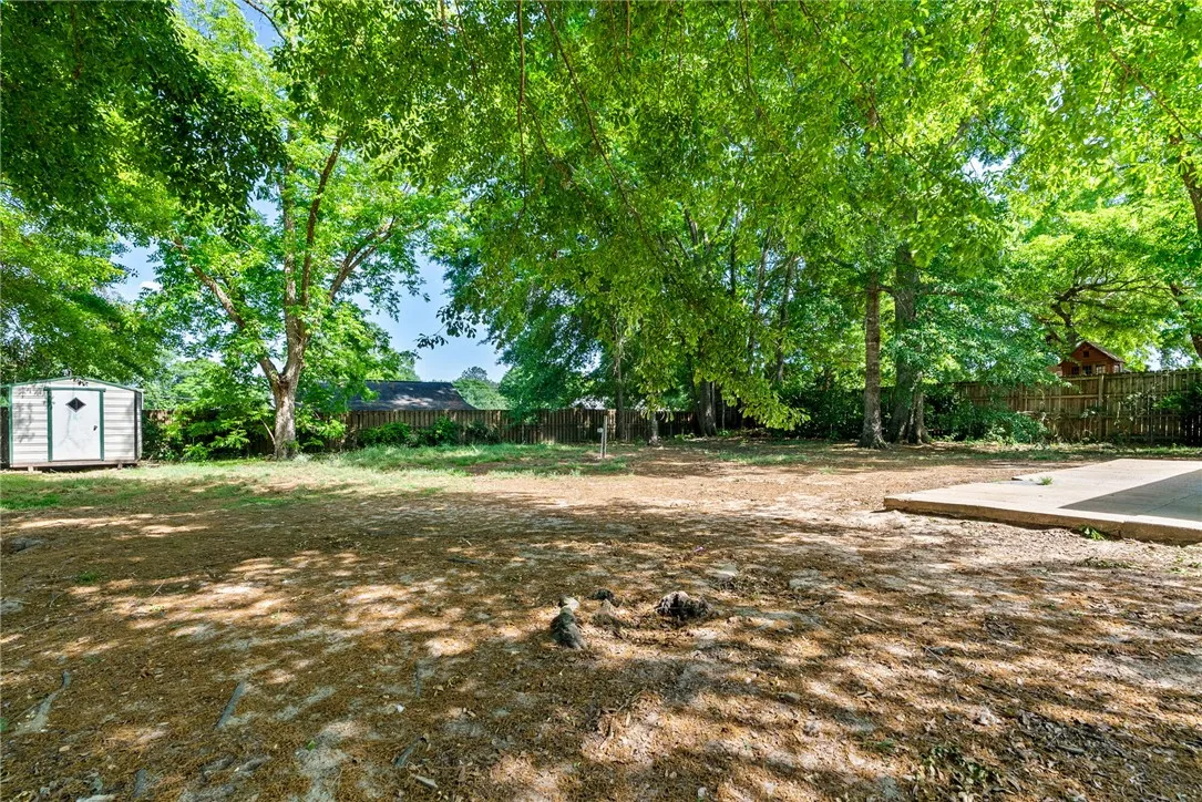 This spacious yard offers a tranquil outdoor space with mature trees and a storage shed.