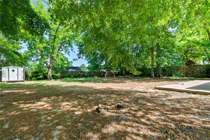This spacious yard offers a tranquil outdoor space with mature trees and a storage shed.