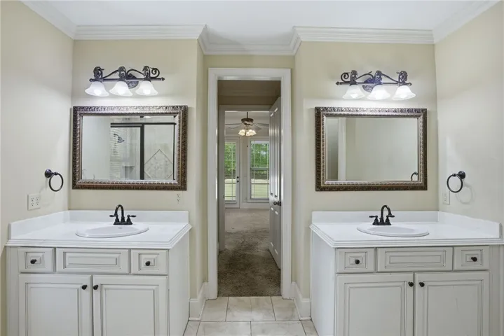 This spacious bathroom offers dual vanities with elegant fixtures and easy access to an adjoining room.