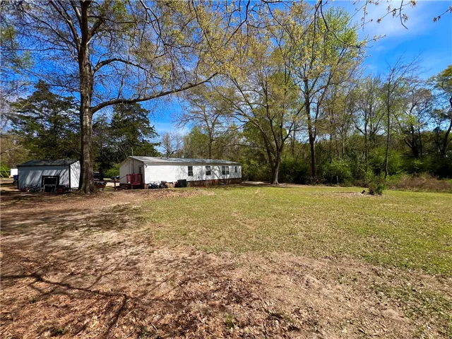 This expansive yard features a charming home and versatile outbuilding amidst lush greenery.