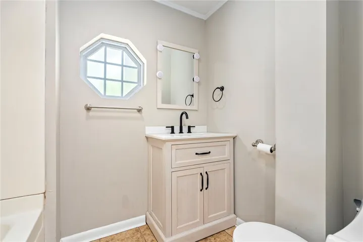 This functional bathroom features a single vanity, a window, and durable tile flooring for easy maintenance.