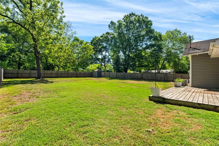 A spacious, verdant yard with mature trees offers a private outdoor retreat with a wooden deck.