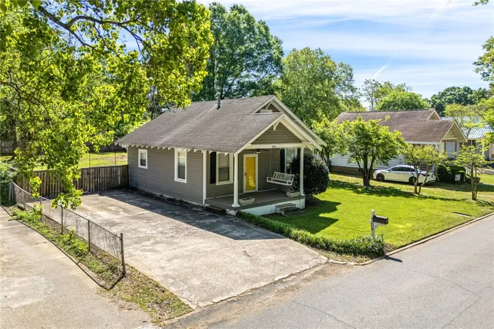 This charming home features a welcoming porch swing, mature trees, and a well-maintained lawn.