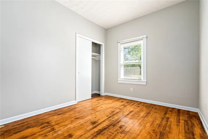 This sunlit room features rich hardwood flooring and a convenient closet, offering a blank canvas for personalization.