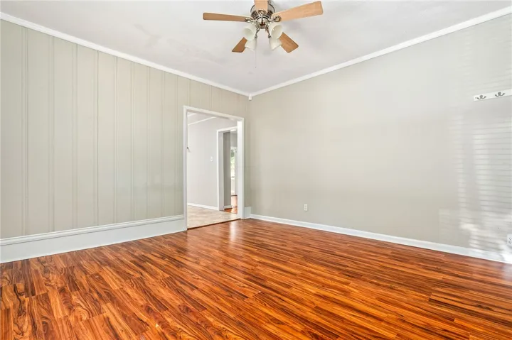 This inviting space features lustrous wood flooring, a ceiling fan, and ample natural light, creating an airy ambiance.