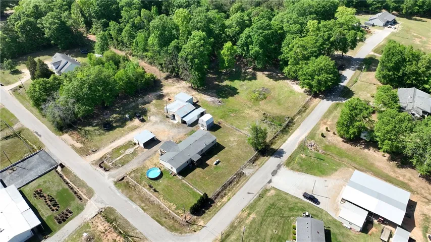 An aerial view showcases a spacious lot with a home, outbuildings, and mature trees.