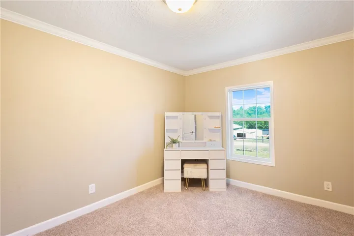 This bright room features soft carpeting and elegant crown molding, creating a cozy and inviting atmosphere.