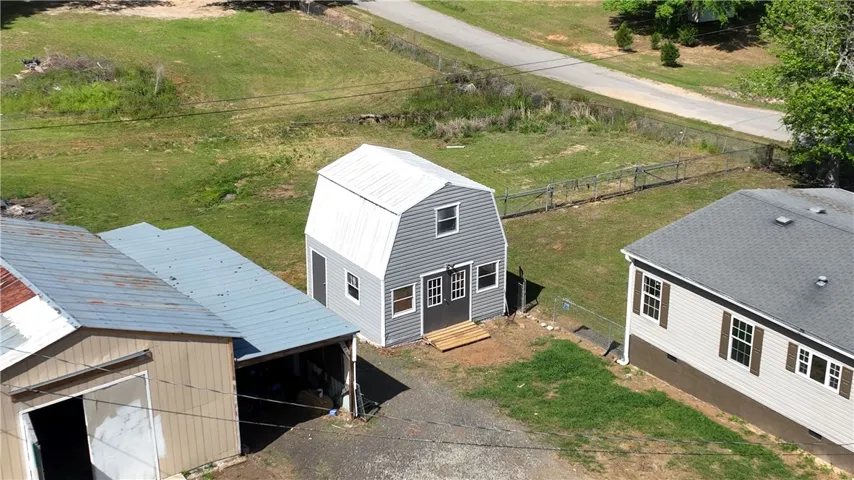 This aerial view showcases a property with diverse structures, a paved driveway, and expansive green space.