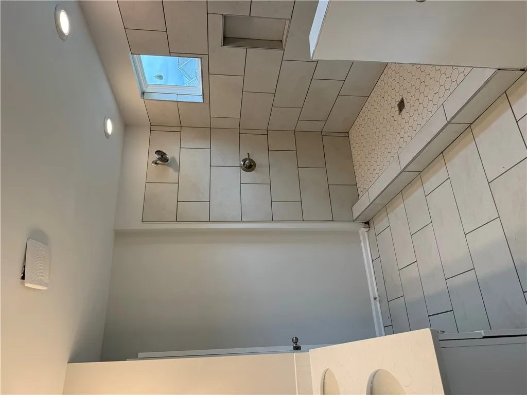 A well-lit primary bathroom with sleek tiling and a functional skylight, offering natural illumination.
