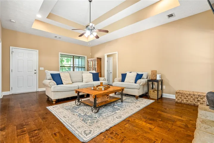 This living room features rich wood flooring, ample natural light, and a tray ceiling with a fan.