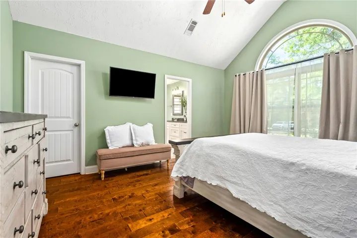 This primary bedroom offers warm hardwood floors, high ceilings, and a view of the ensuite bathroom.
