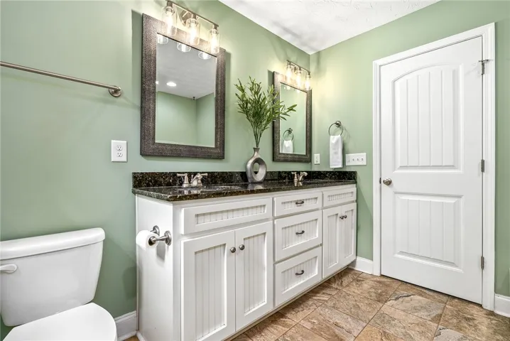 This bathroom features a double vanity with granite counters and durable tile flooring.