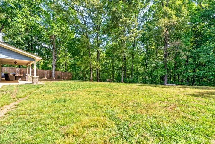 This expansive yard features a charming covered patio and a lush, wooded backdrop.