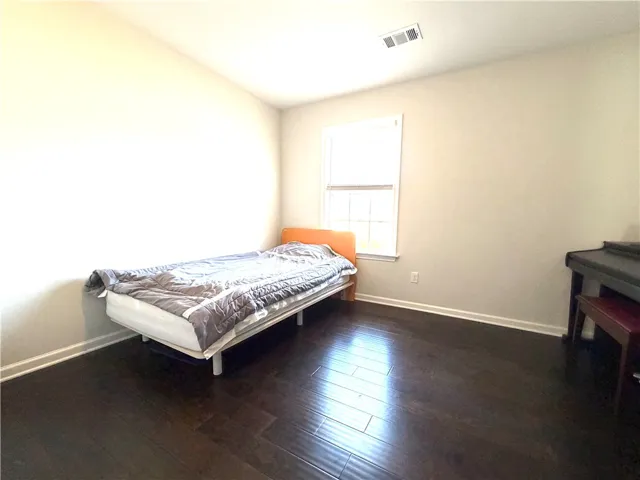 This airy bedroom features rich hardwood flooring and a bright window, creating a serene personal retreat.