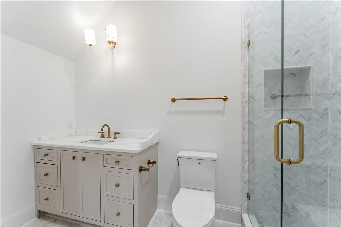 This bright bathroom features a vanity, toilet, and glass-enclosed shower with herringbone tile.