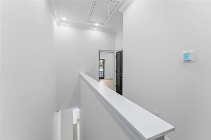 This interior hallway features crisp walls, recessed lighting, and elegant crown molding, leading to additional living spaces.