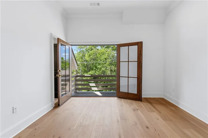 An inviting room features a balcony with lush tree views and rich hardwood flooring.