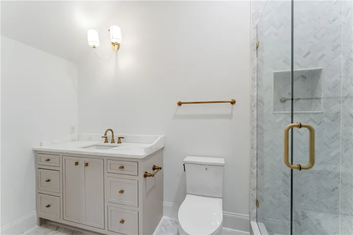 This bright bathroom features a vanity, toilet, and glass-enclosed shower with herringbone tile.
