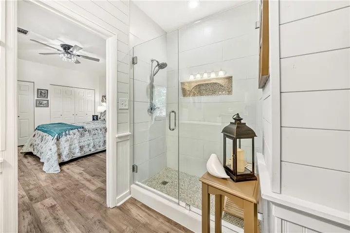 This primary bedroom and bathroom combo features a sleek glass-enclosed shower with mosaic accents.