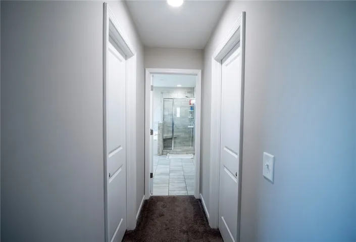 This bright hallway connects to a spacious bathroom with a modern glass shower.