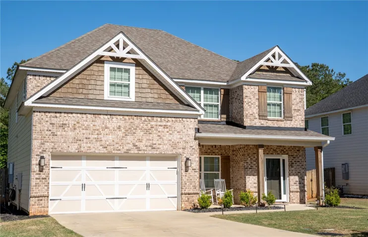 This classic brick and shingle home features an inviting porch and attached garage, offering both curb appeal and functionality.