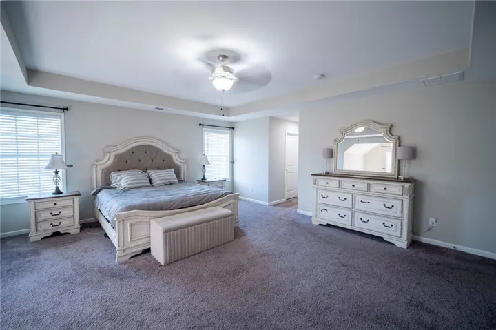 This spacious primary bedroom offers comfort with its carpeted flooring and high ceilings.