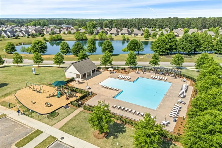 This aerial view showcases a vibrant community pool area with a playground, all set against a tranquil lake.