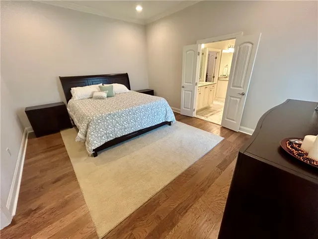 This primary bedroom features elegant wood flooring, crown molding, and an adjoining bathroom.