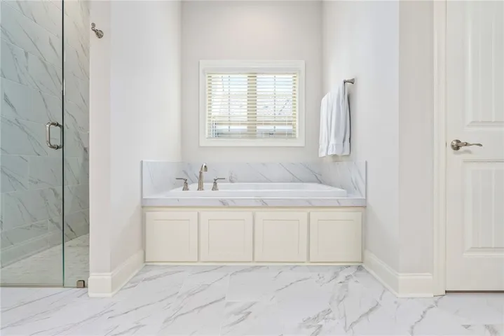 This serene bathroom offers a spacious soaking tub and a sleek glass-enclosed shower.