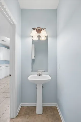 This half bathroom features a simple pedestal sink and a well-lit mirror. Perfect for guests.