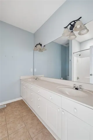 This primary bathroom offers dual sinks, ample storage, and a shower for everyday convenience.