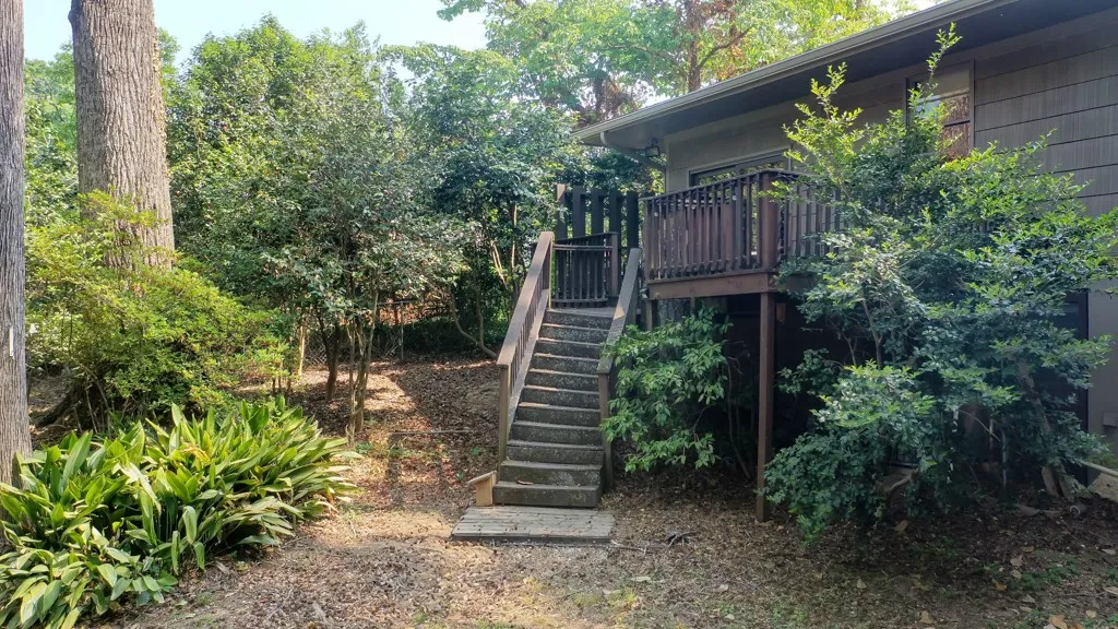 This property features an inviting deck with stairs, surrounded by lush, mature greenery.