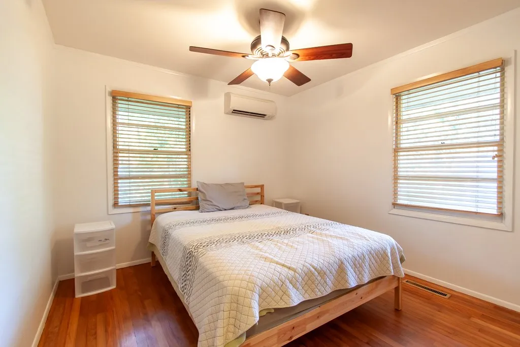 This cozy bedroom offers rich hardwood floors and abundant natural light through large windows.