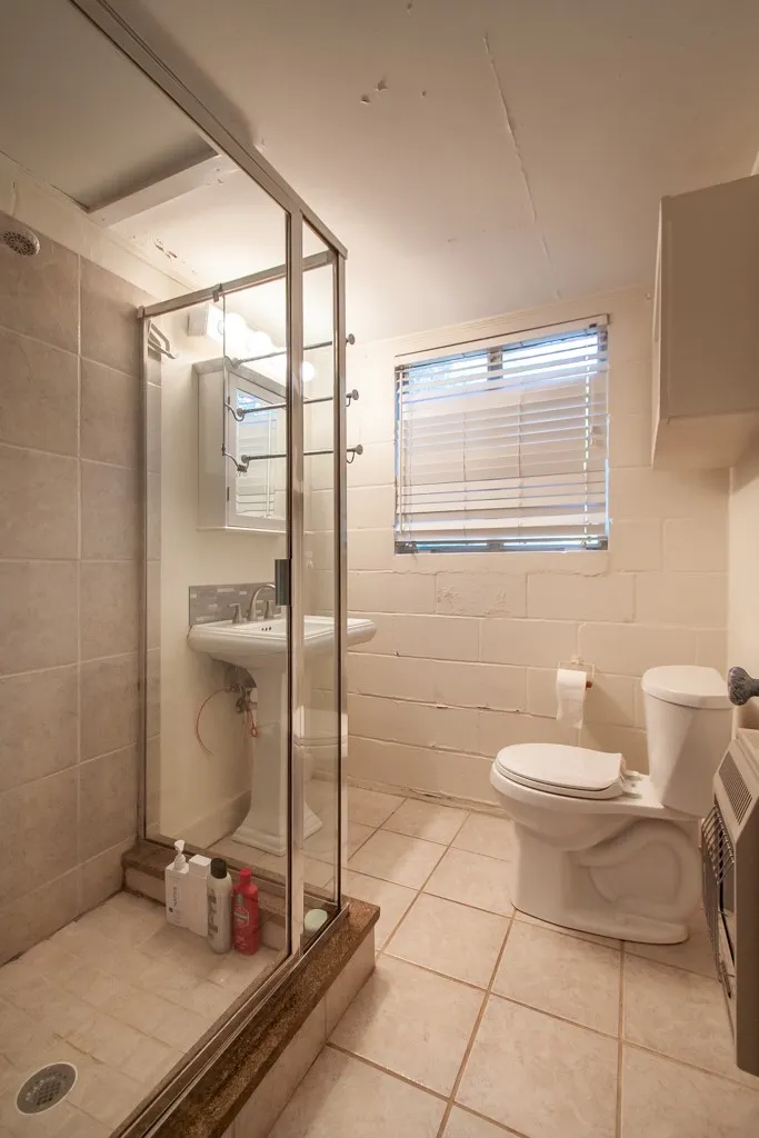 This functional bathroom features a tiled shower and pedestal sink, offering practicality and ease.