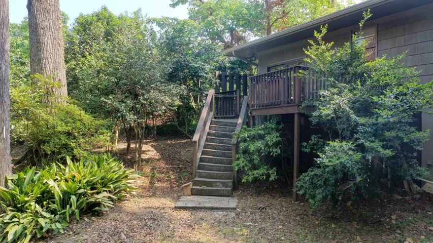 This property features an inviting deck with stairs, surrounded by lush, mature greenery.