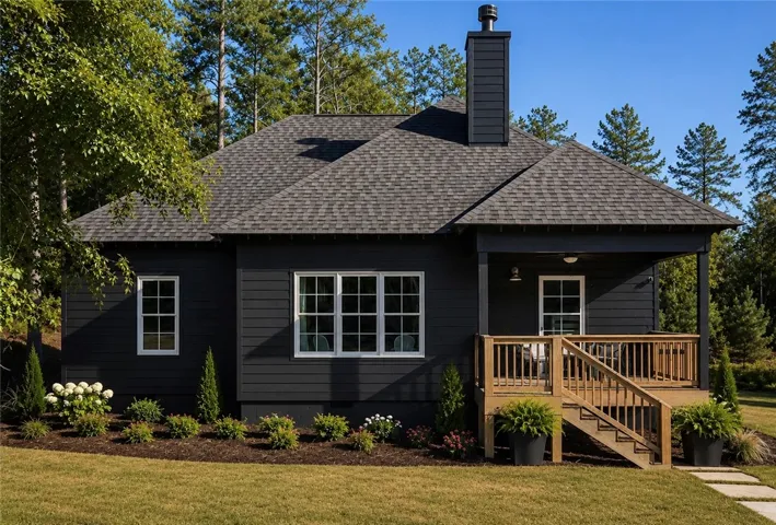 A charming dark-clad home features a welcoming wooden deck and thoughtfully designed landscaping, nestled amongst towering trees.