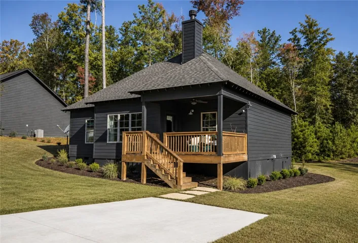 A dark-toned dwelling featuring a covered deck and steps leading to a concrete patio, nestled among mature trees.