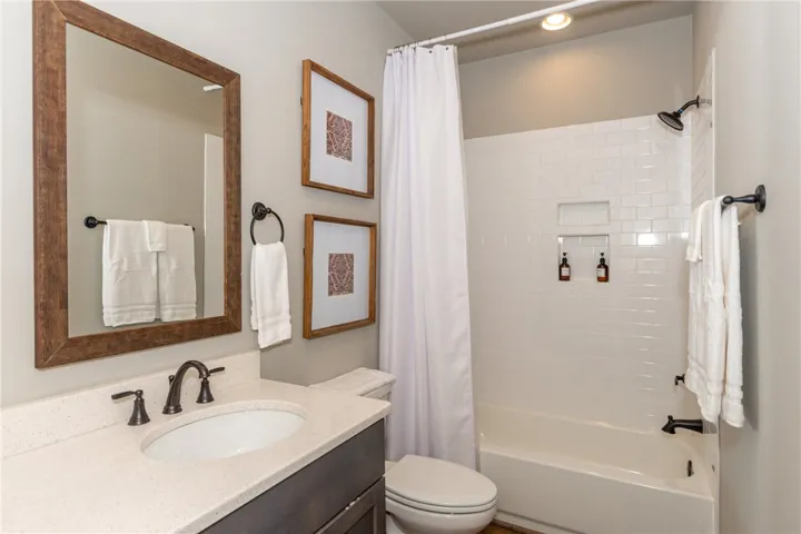 This clean and bright bathroom features a vanity, toilet, and a tiled shower with a tub.