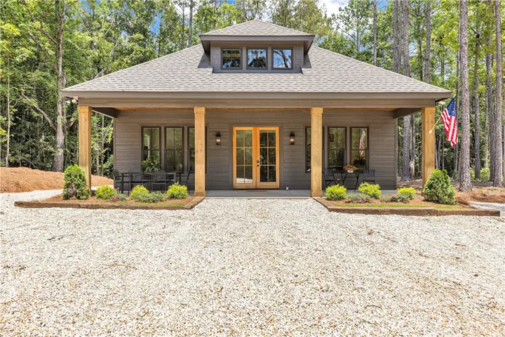 A secluded retreat featuring a gravel driveway, inviting front porch, and dormer window, surrounded by a peaceful forest.