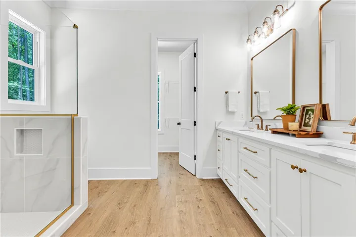 White cabinetry with gold hardware provides ample storage space in this well-appointed primary bathroom.