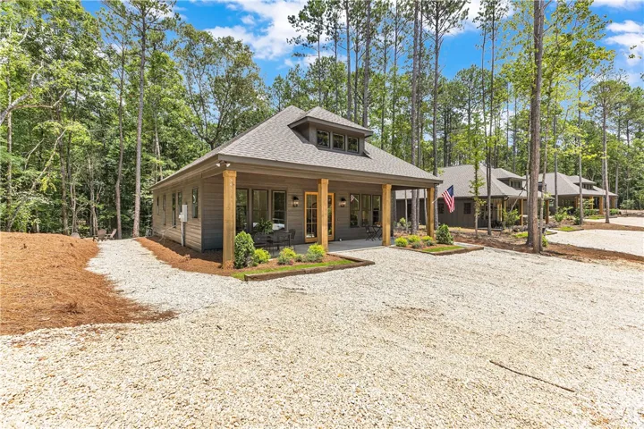 A charming cottage-style residence nestled among tall trees, featuring a welcoming covered porch and durable shingle roofing.